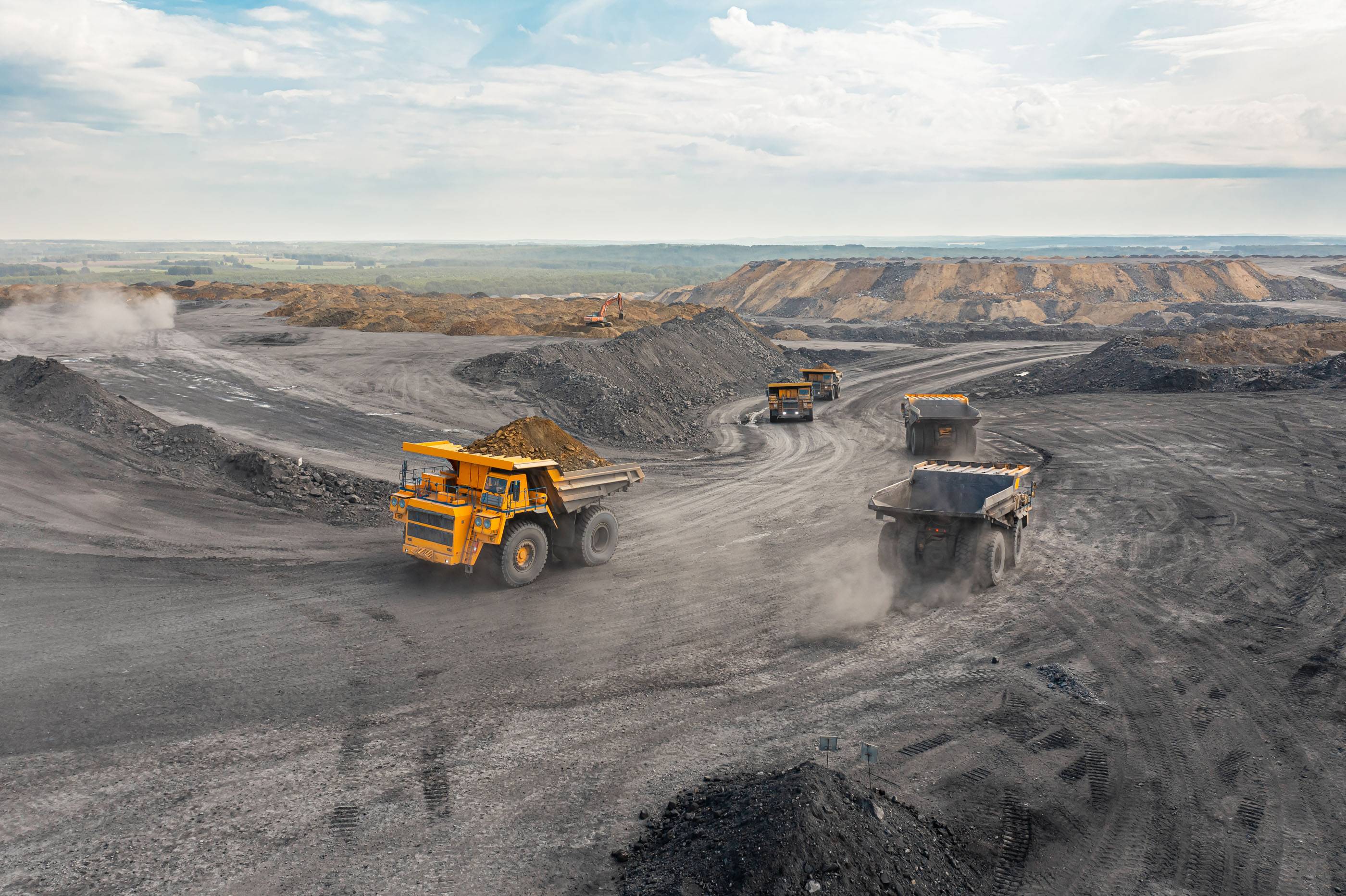 Большой карьерный самосвал. Большой желтый горный грузовик на рабочей площадке. Загрузка угля в кузов самосвала. Добыча полезных ископаемых. Карьерная техника для транспортировки угля из разреза.