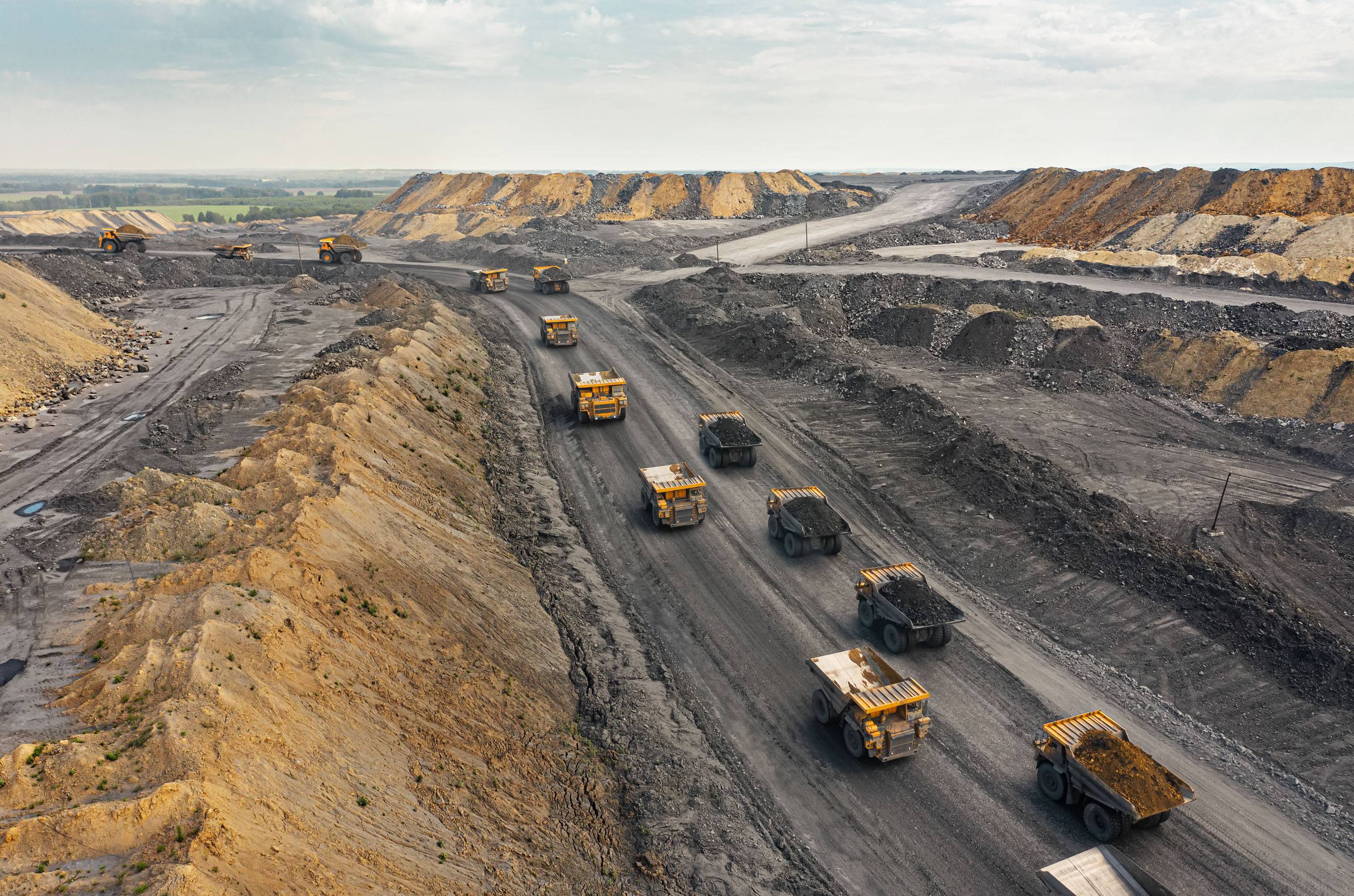 Большой карьерный самосвал. Большой желтый горный грузовик на рабочей площадке. Загрузка угля в кузов самосвала. Добыча полезных ископаемых. Карьерная техника для транспортировки угля из разреза.