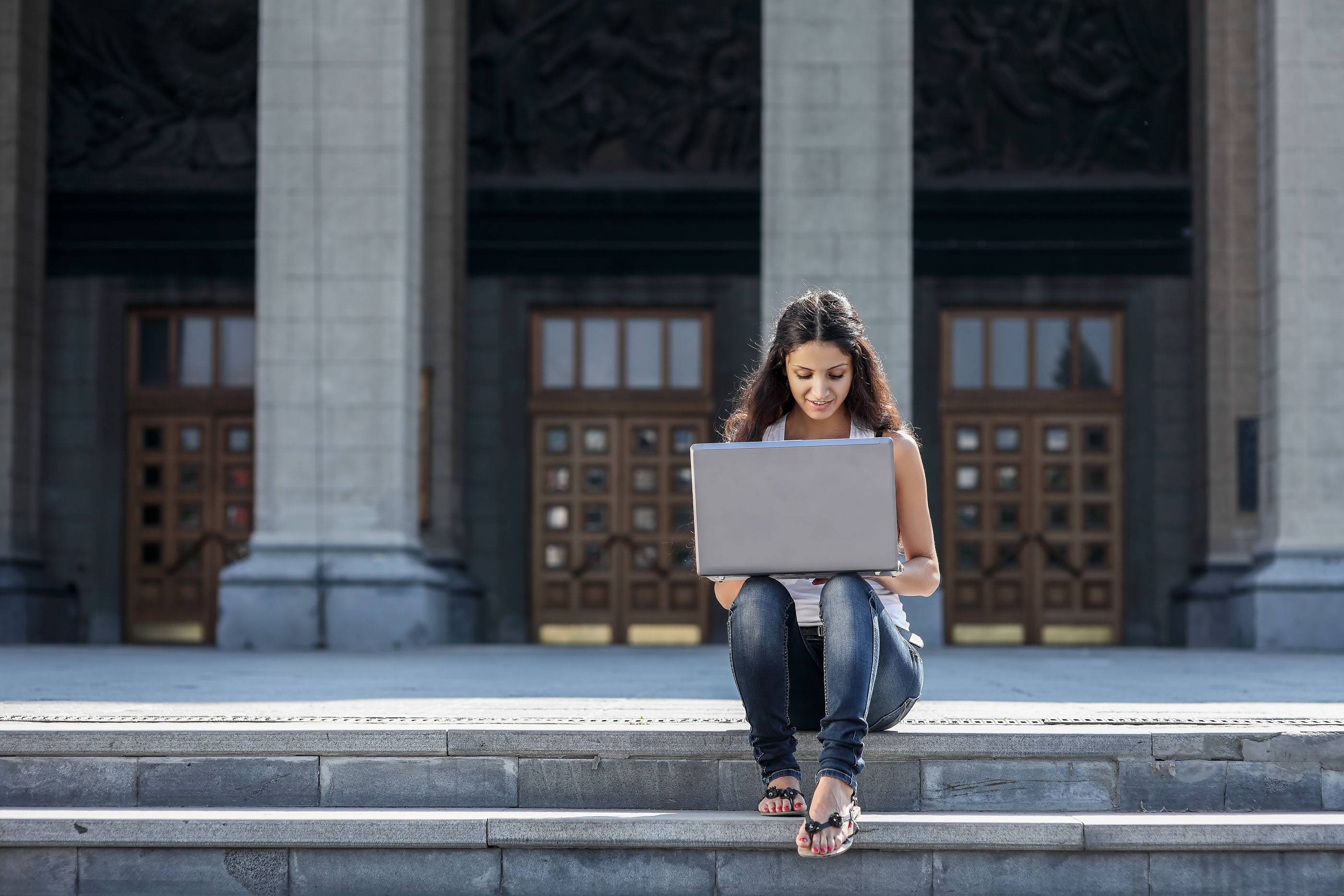 Молодая женщина с ноутбуком сидит на лестнице рядом с университетом