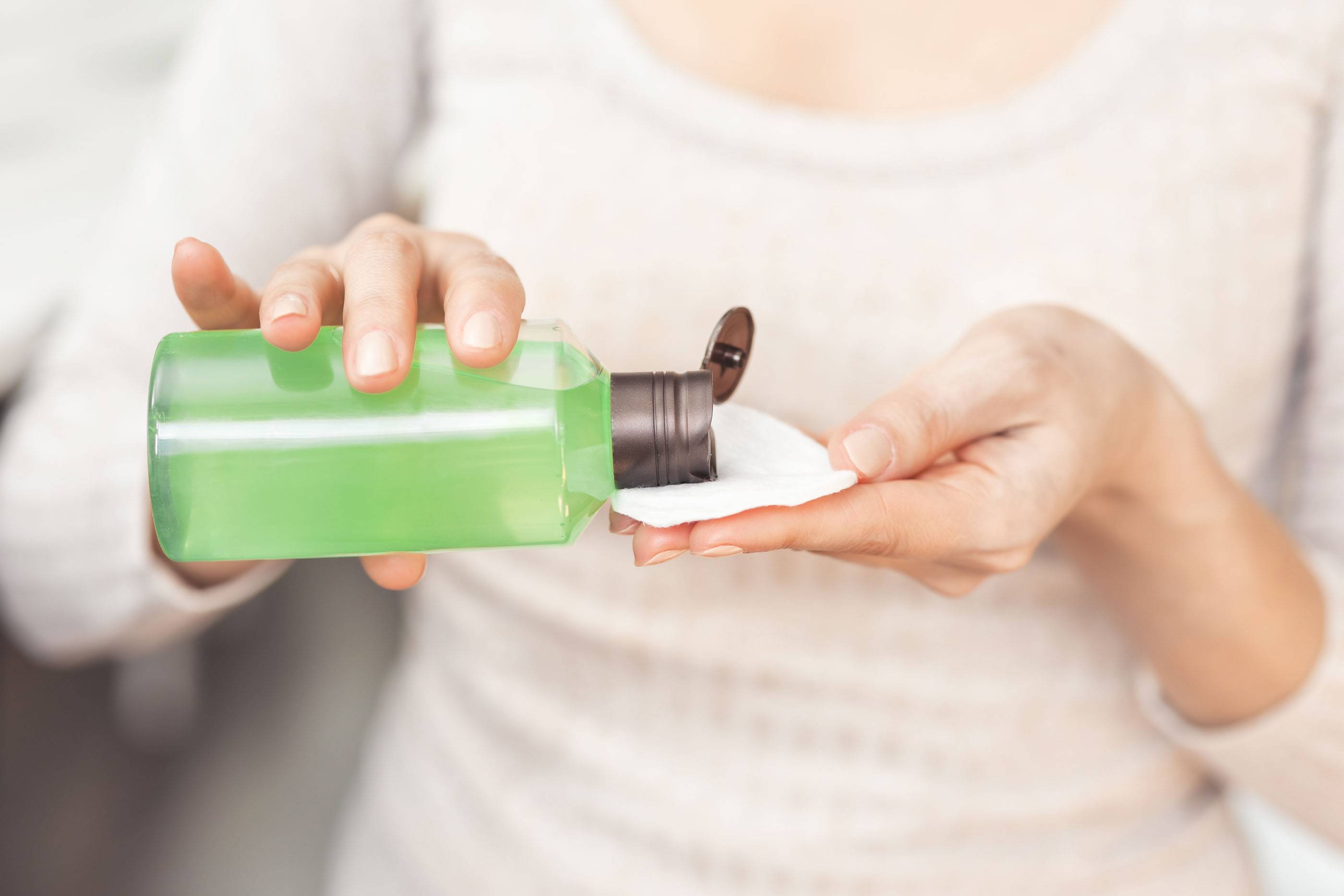 Снятие макияжа и уход за кожей. Крупный план: женщина держит ватный диск и средство для снятия макияжа. Очищение лица лосьоном. Женщина с флаконом косметического средства.