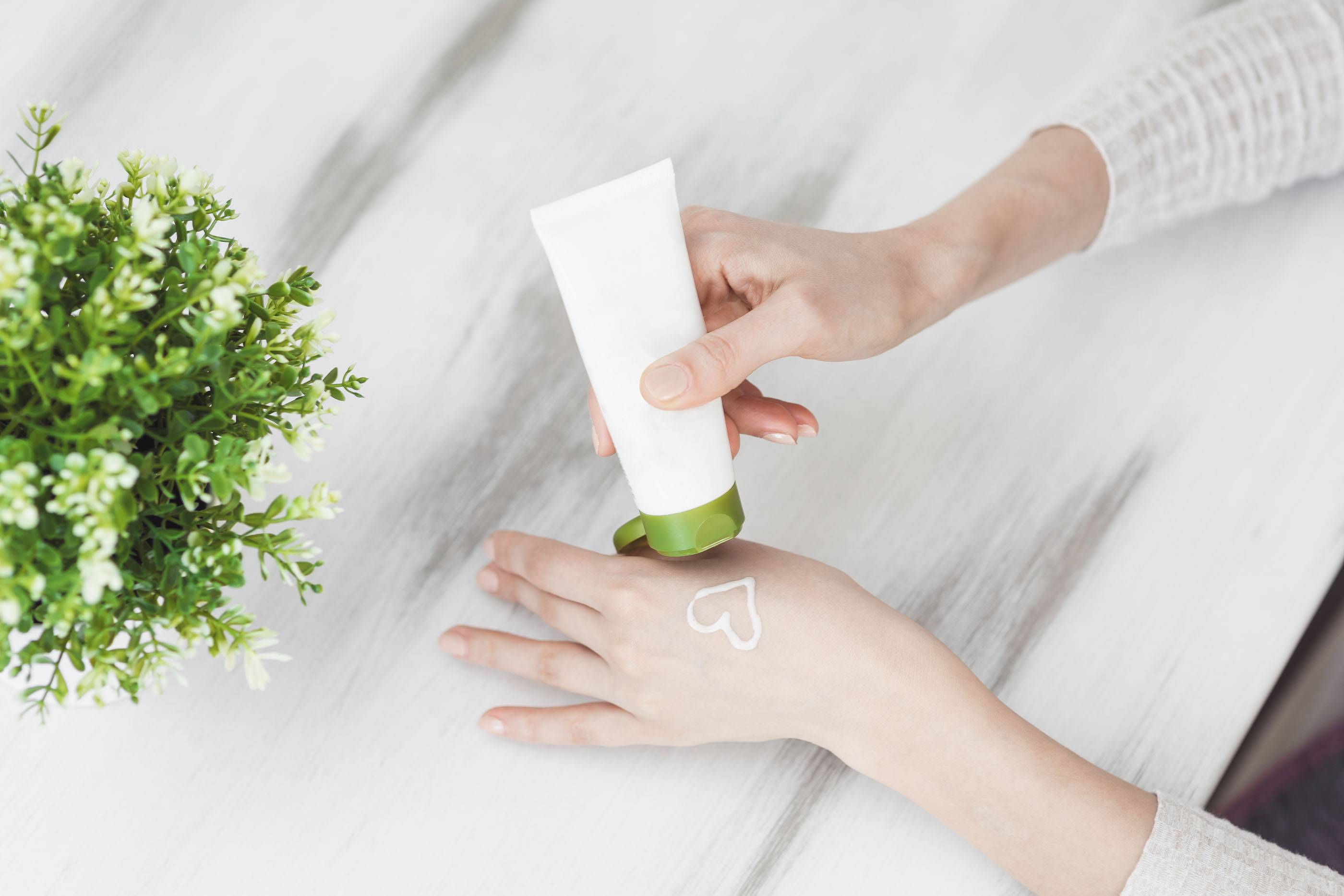 Вид сверху. Крем для ухода за кожей рук. Крупный план: женщина с кремом для рук. Женщина наносит крем для рук. Девушка держит тюбик со средством для ухода за кожей.