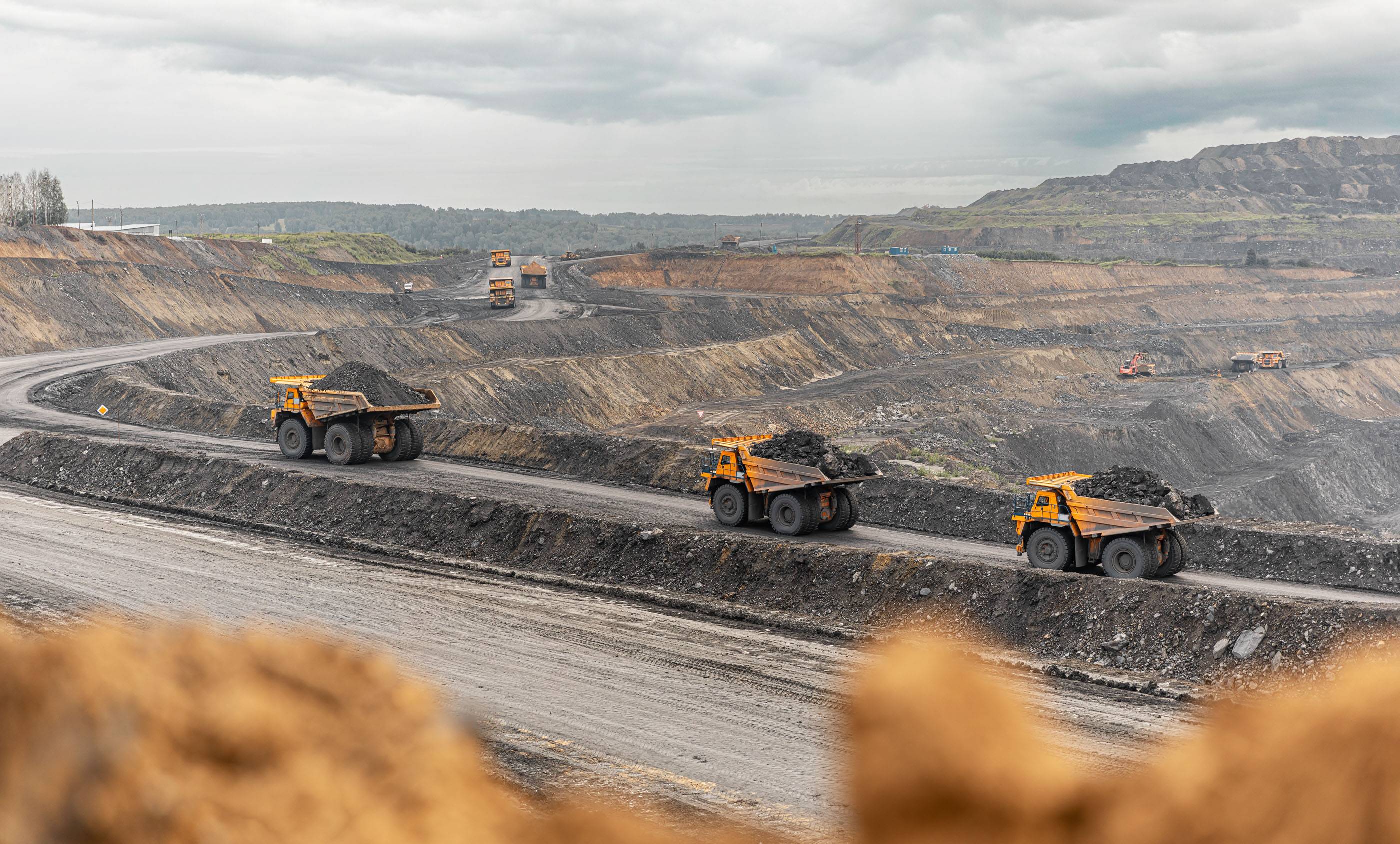 Большой карьерный самосвал. Большой желтый горный грузовик на рабочей площадке. Загрузка угля в кузов самосвала. Добыча полезных ископаемых. Карьерная техника для транспортировки угля из разреза.