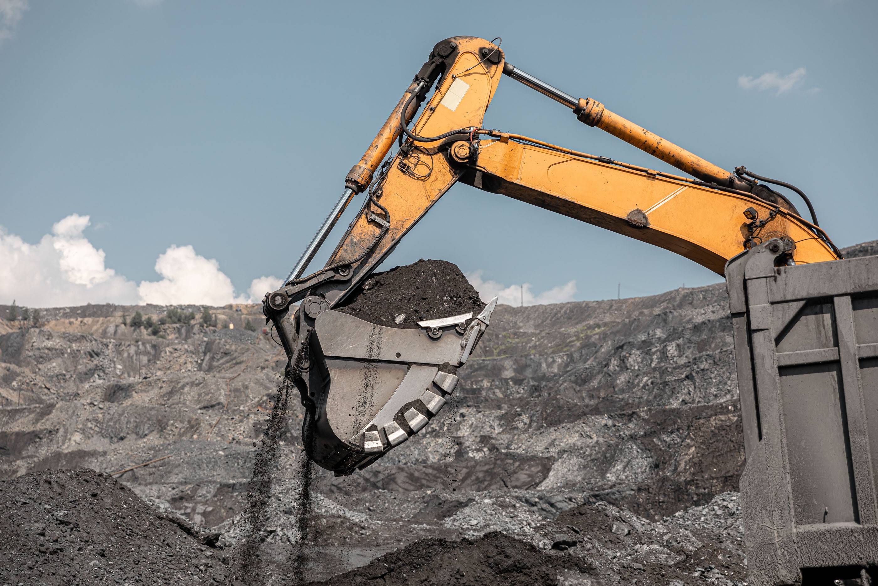 Большой карьерный экскаватор. Большой желтый горный экскаватор на рабочем месте. Загрузка угля в кузов самосвала. Карьерный экскаватор, горная техника для погрузки породы. Добыча полезных ископаемых.