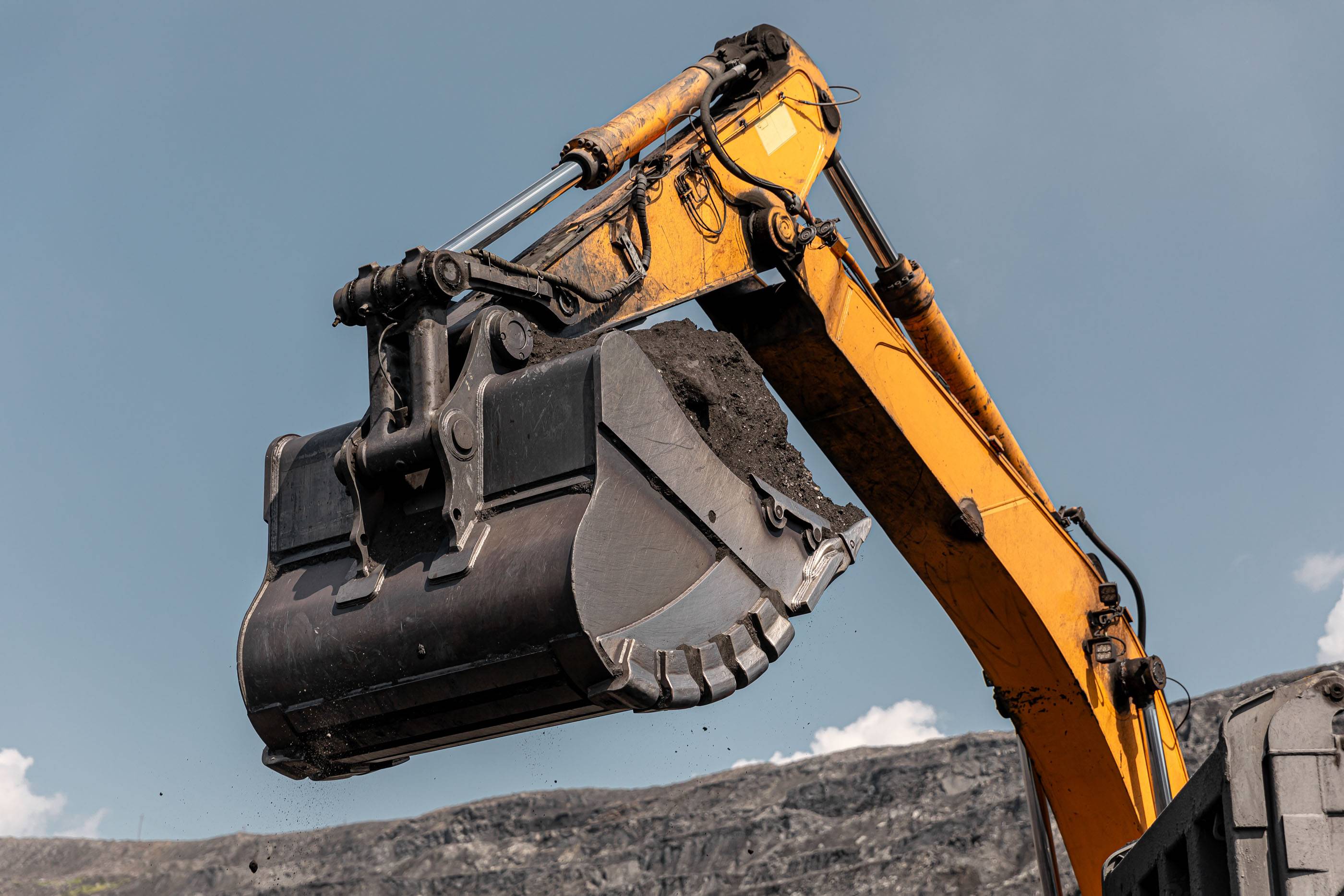 Стрела экскаватора с гидравлическим ковшом. Большой желтый карьерный экскаватор. Крупный карьерный самосвал на угольном месторождении. Погрузка угля в грузовик. Карьерная техника для транспортировки угля из разреза.