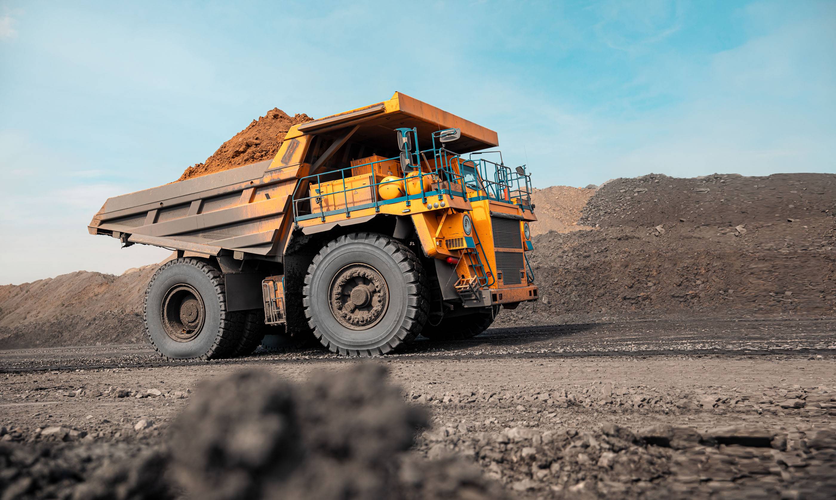 Большой карьерный самосвал. Большой желтый горный грузовик на рабочей площадке. Загрузка угля в кузов самосвала. Добыча полезных ископаемых. Карьерная техника для транспортировки угля из разреза.