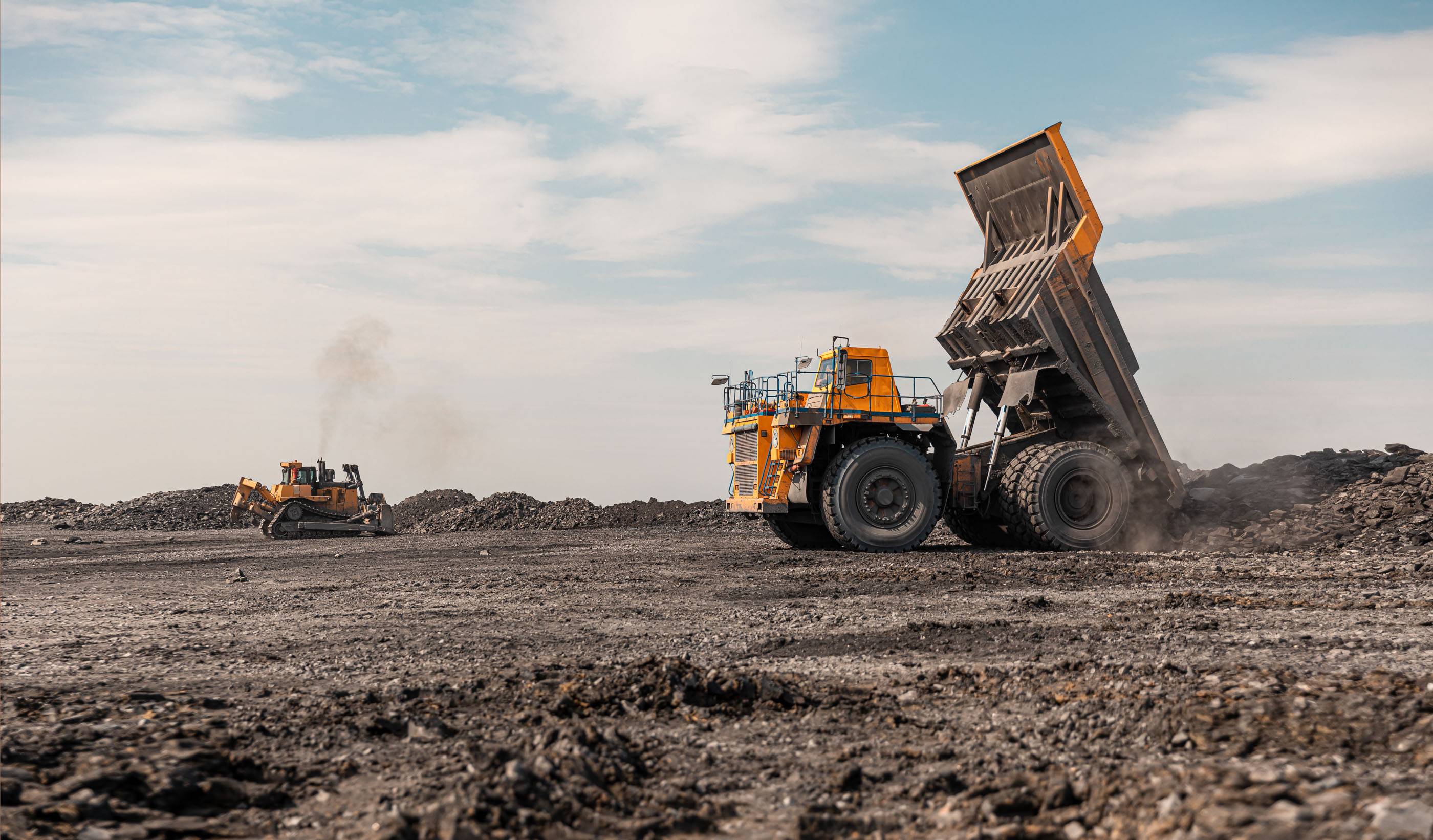 Большой карьерный самосвал. Большой желтый горный грузовик на рабочей площадке. Загрузка угля в кузов самосвала. Добыча полезных ископаемых. Карьерная техника для транспортировки угля из разреза.