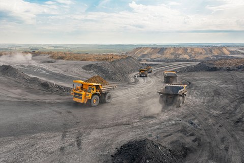 Большой карьерный самосвал. Большой желтый горный грузовик на рабочей площадке. Загрузка угля в кузов самосвала. Добыча полезных ископаемых. Карьерная техника для транспортировки угля из разреза.