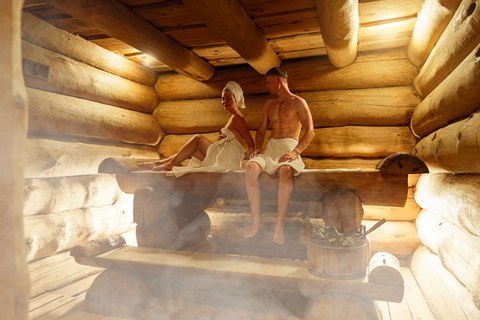 Молодая пара отдыхает и потеет в жаркой сауне, завернутая в полотенца. Мужчина и женщина в сауне. Интерьер финской сауны, классическая деревянная парная. Русская баня.