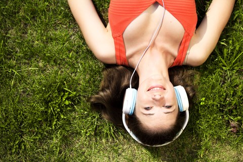 Молодая женщина в наушниках на зеленой траве в парке