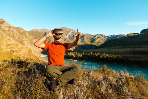 Успешный молодой человек использует VR-очки для виртуальной экскурсии в горах во время летнего отпуска