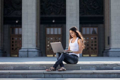 Молодая женщина с ноутбуком сидит на лестнице рядом с университетом