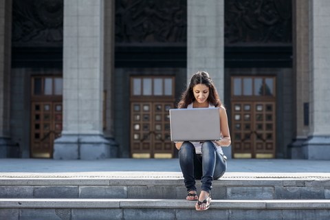 Молодая женщина с ноутбуком сидит на лестнице рядом с университетом