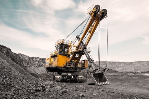 Большой карьерный экскаватор. Крупная желтая выемочная машина на объекте. Погрузка угля в кузов грузовика. Добыча полезных ископаемых. Карьерная техника для транспортировки угля из разреза